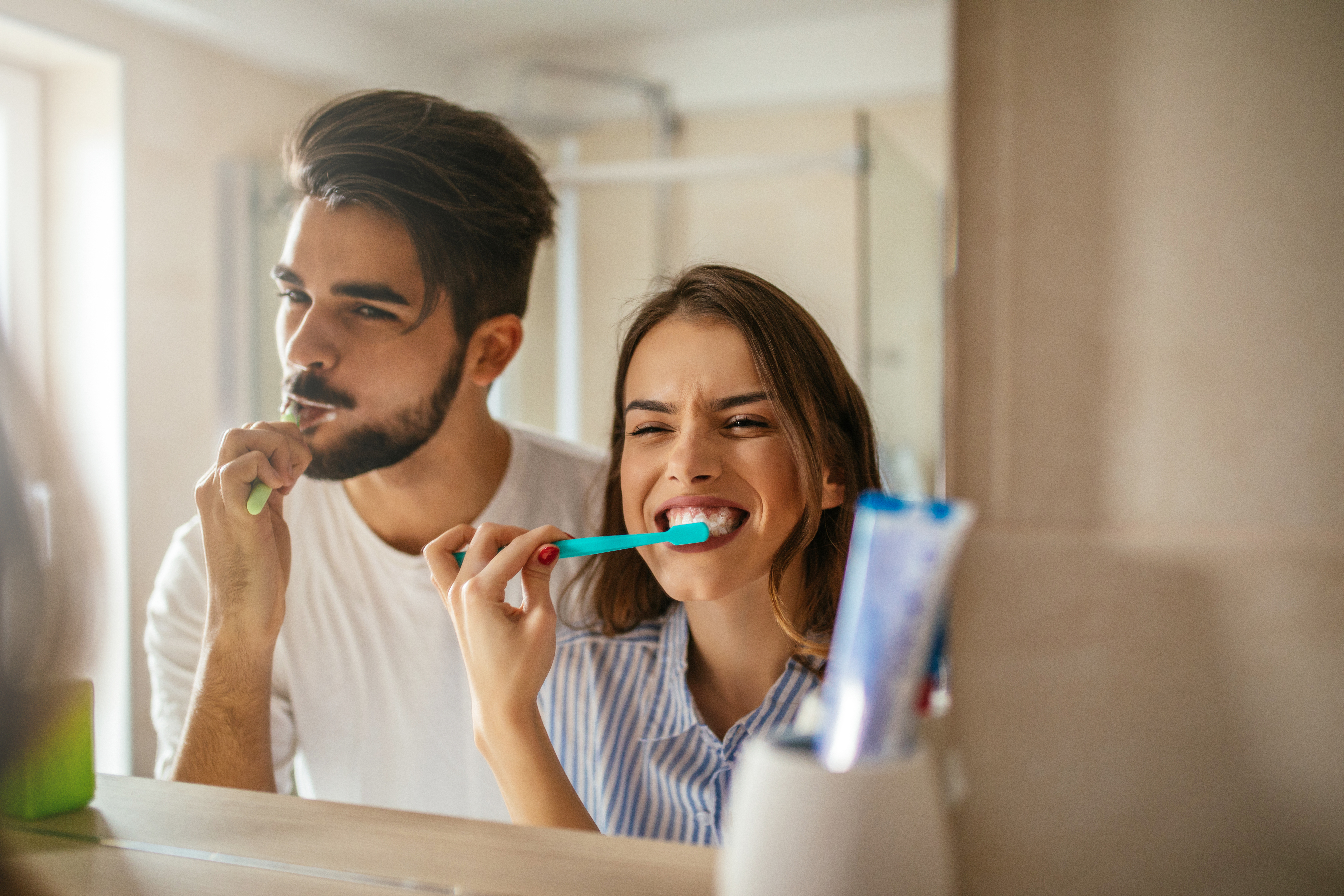 Young couple brush their teeth with baking soda toothpaste in front of a mirror