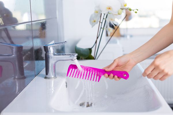 Woman rinsing a pink hair comb in the sink.
