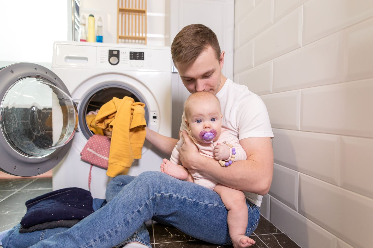 New dad holding baby while washing new baby clothes