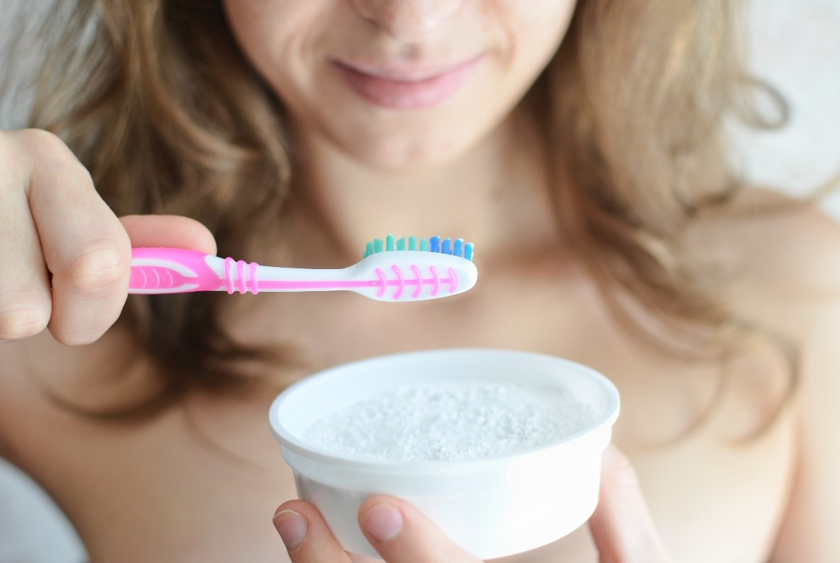 Young woman brushes with arm and hammer baking soda to help whiten her teeth