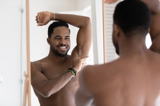 man smiling in mirror applying deodorant under arm