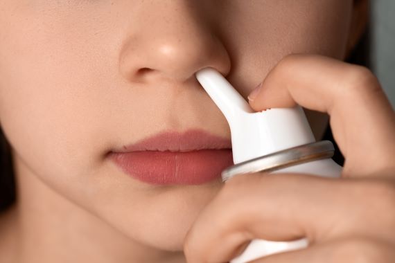 Girl inserting the tip of a saline spray bottle into nostril to irrigate the nose.